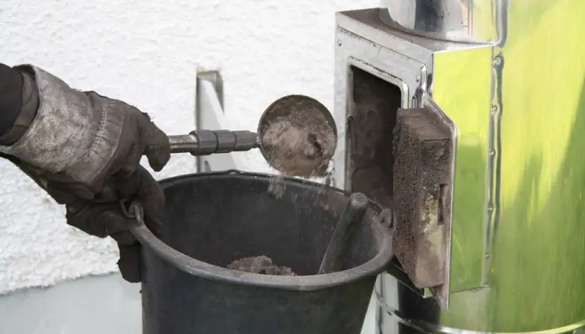 Rękawica zrzuca sadzę do wiadra. Czyszczenie komina od dołu to ważny etap dbania o bezpieczeństwo.