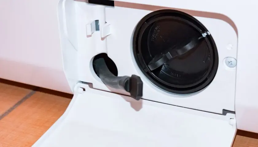 Otwarta klapka z wężykiem do spuszczania wody i czarną zakrętką filtra. Dowiedz się, jak wyczyścić filtr w pralce Whirlpool, aby zapewnić jej sprawność.