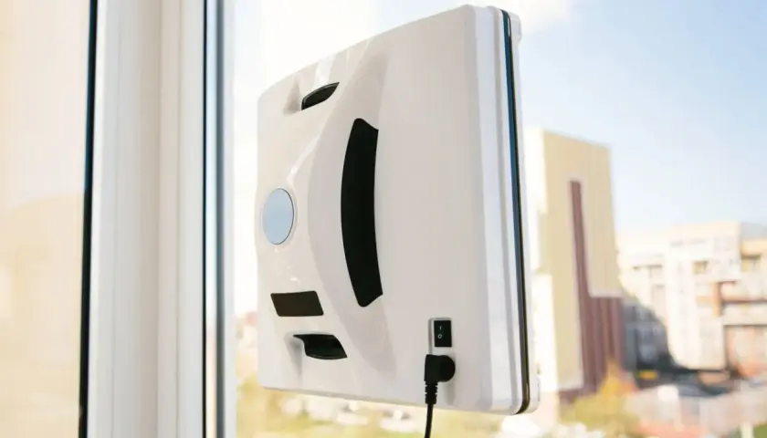 Biały robot do mycia okien przyczepiony do szyby. To urządzenie może być częścią rankingu robotów do mycia okien, ułatwiając czyszczenie.
